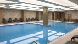 A modern indoor swimming pool with lounge chairs and a tiled floor.