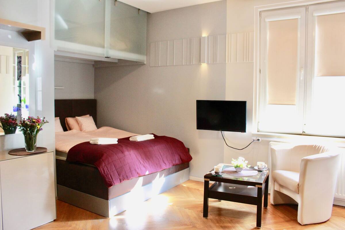A modern bedroom with a bed, bedside table, chair, and a TV mounted on the wall.