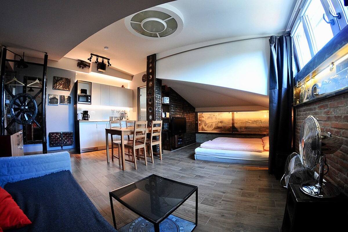 A compact living space with a kitchen, dining area, and a loft bedroom with a brick wall and a bed.