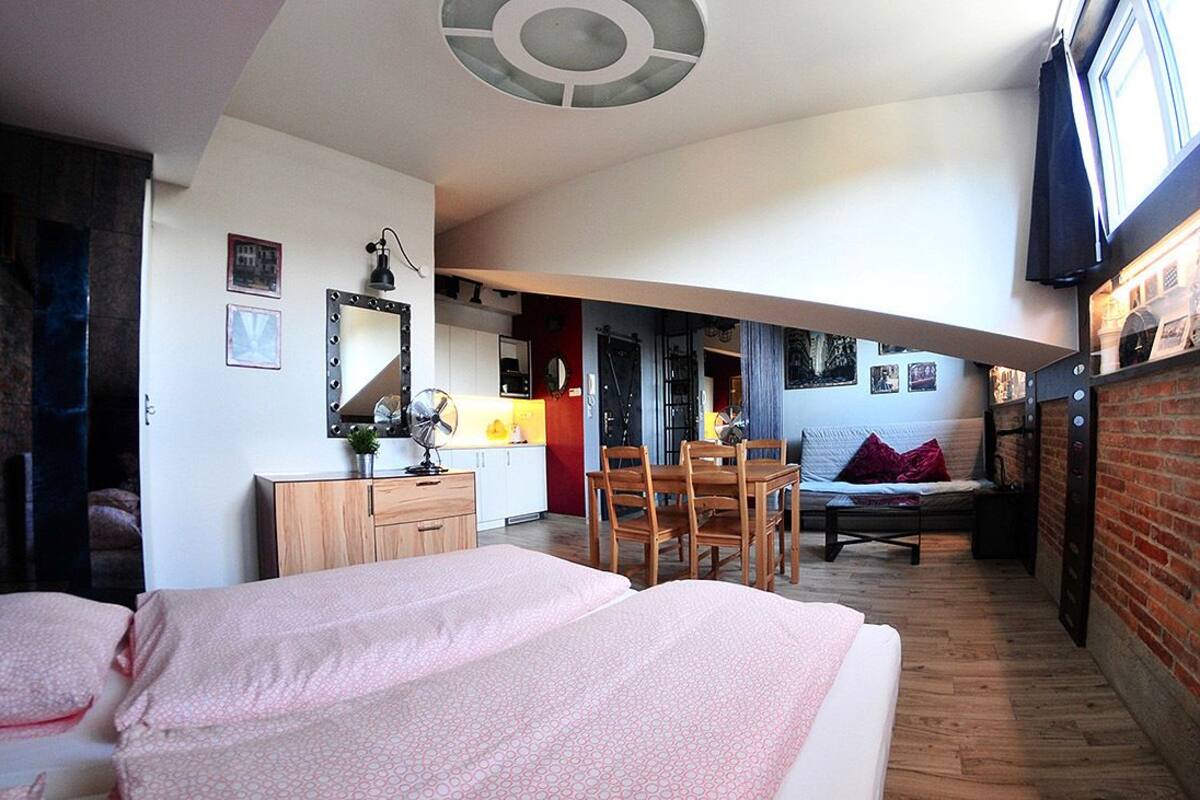 A compact hotel room with a bed, a small desk, a chair, and a dining table.