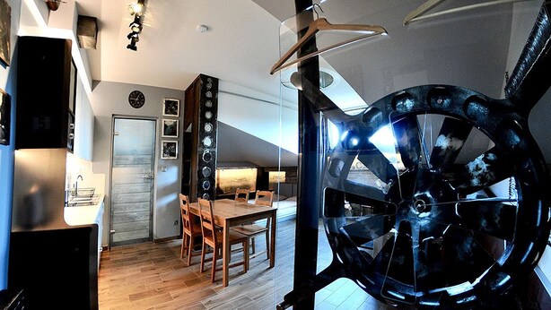 Une cuisine moderne avec un plancher en bois, un coin repas avec une table et des chaises, et une grande structure circulaire de couleur sombre au premier plan.