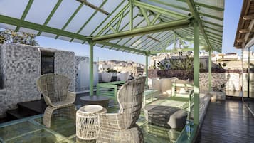 A covered outdoor seating area with wicker furniture and a glass table, overlooking a cityscape.
