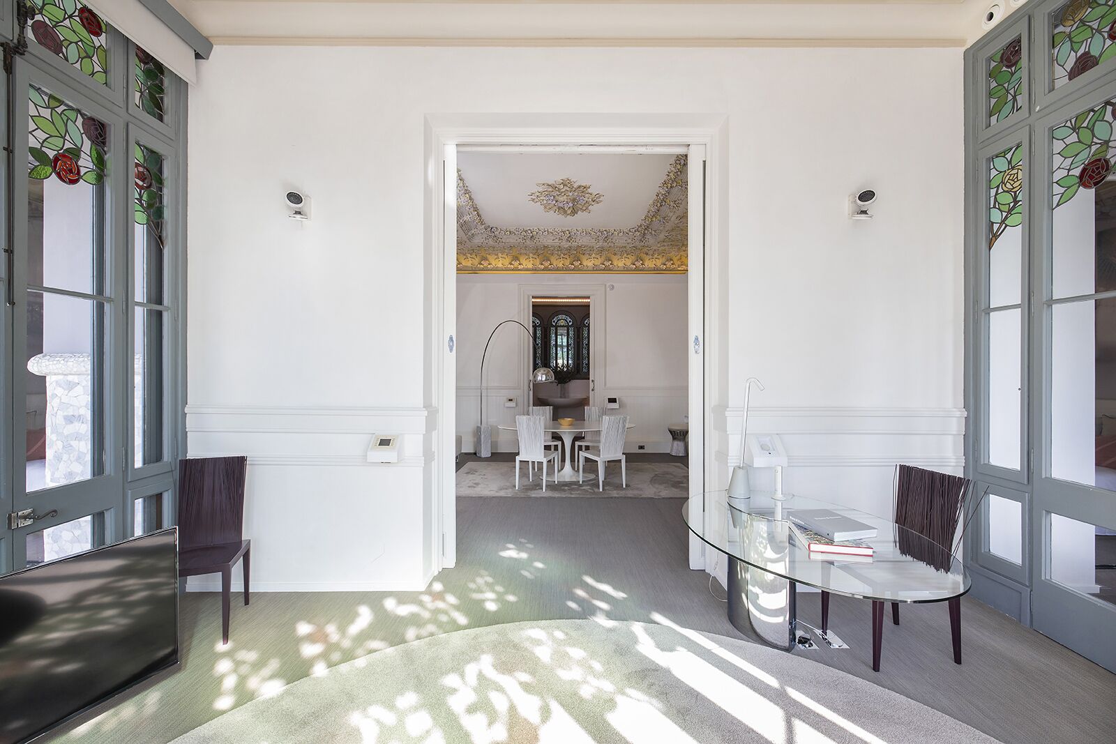 A hallway with a dining area in the background, featuring a chandelier and a table with chairs.
