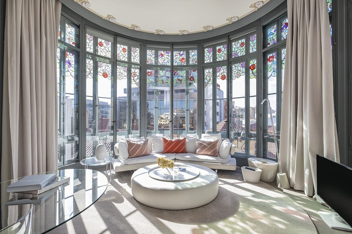 Un salon moderne doté d’un mur en verre incurvé, d’un ensemble de canapés blancs, d’une table basse ronde et offrant une vue sur le paysage urbain.