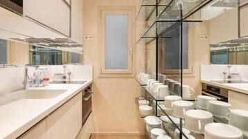 A modern bathroom with a large mirror, a sink, and a glass shelf with neatly arranged plates and cups.
