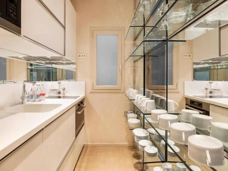A modern bathroom with a large mirror, a sink, and a glass shelf with neatly arranged plates and cups.
