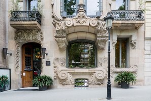 Ein historisches Gebäude mit aufwendigen architektonischen Verzierungen, einem großen Bogenfenster und einer Tafel mit dem Namen 'EL PALAET'.