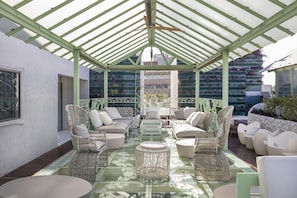 A covered outdoor seating area with wicker furniture and a glass table.