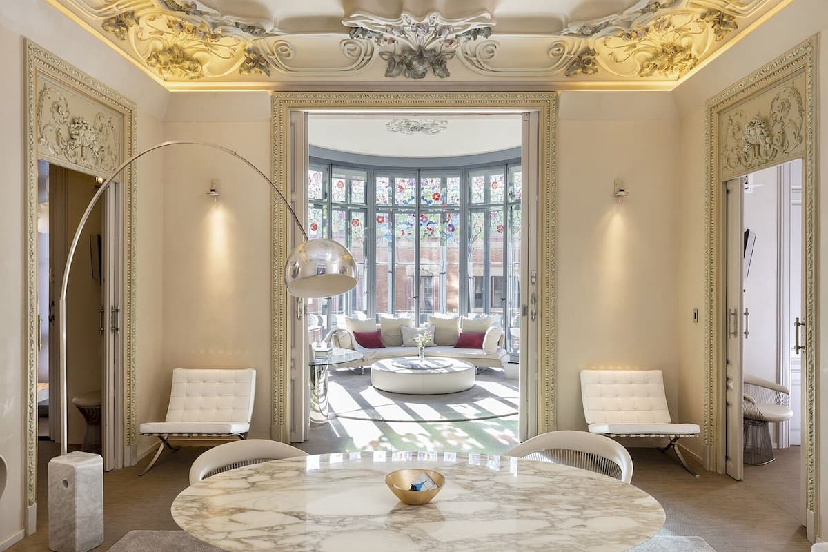 Une chambre luxueuse dotée d’un sol en marbre, d’une table ronde avec un récipient, et d’un coin salon comprenant un canapé et des fauteuils.