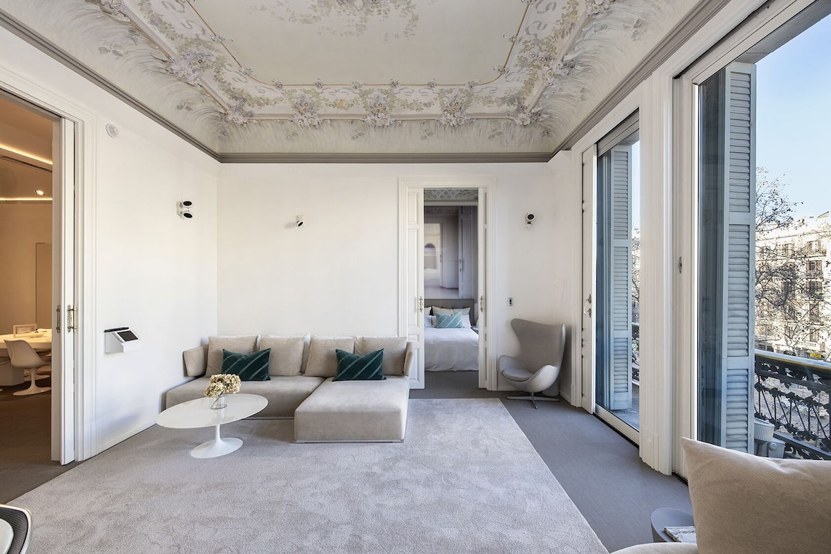 Un salon spacieux avec un canapé moderne, une petite table ronde et un fauteuil. Il y a un balcon avec une balustrade et une vue sur la ville.