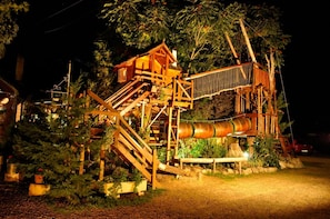 A wooden treehouse with a spiral staircase and a rope bridge, surrounded by lush greenery.