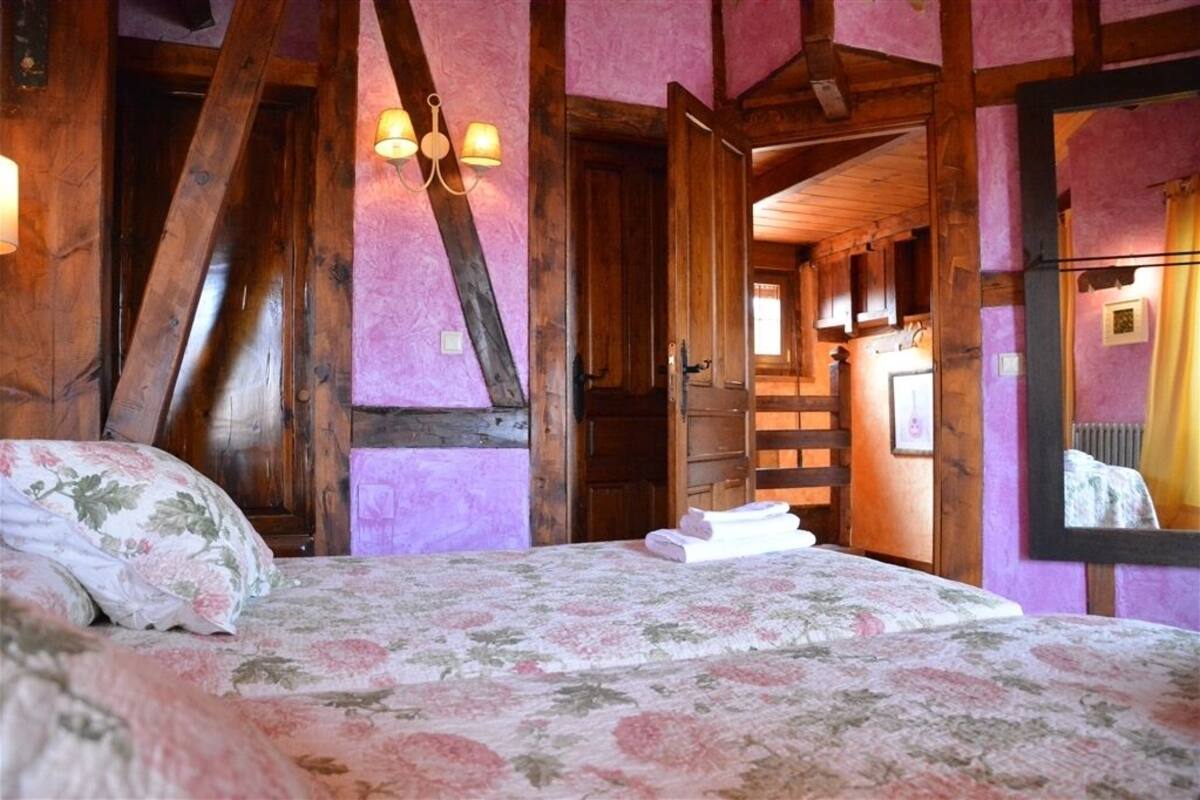 Een slaapkamer met een houten plafond, een bed met bloemenbeddengoed en een kroonluchter.