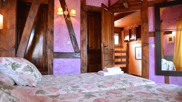 Une chambre avec un plafond en bois, un lit recouvert d’une literie à motifs floraux et un lustre.