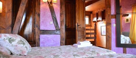 Une chambre avec un plafond en bois, un lit recouvert d’une literie à motifs floraux et un lustre.