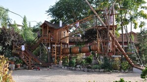 A rustic wooden structure with a staircase, a slide, and a large cylindrical object. - Hospedium Hacienda Las Cavas (Olmedo)