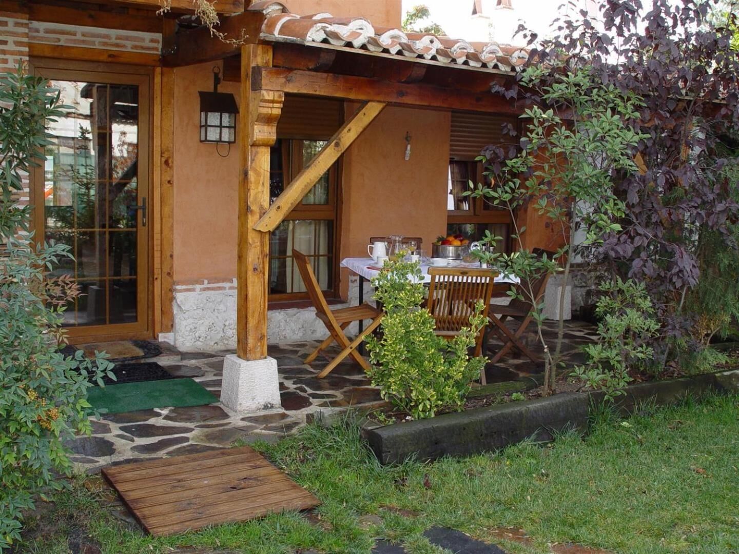 A rustic wooden house with a stone patio, a wooden table with chairs, and a small garden area.