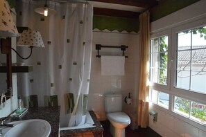 A bathroom with a sink, toilet, and shower curtain. There is a window with a view of greenery outside.