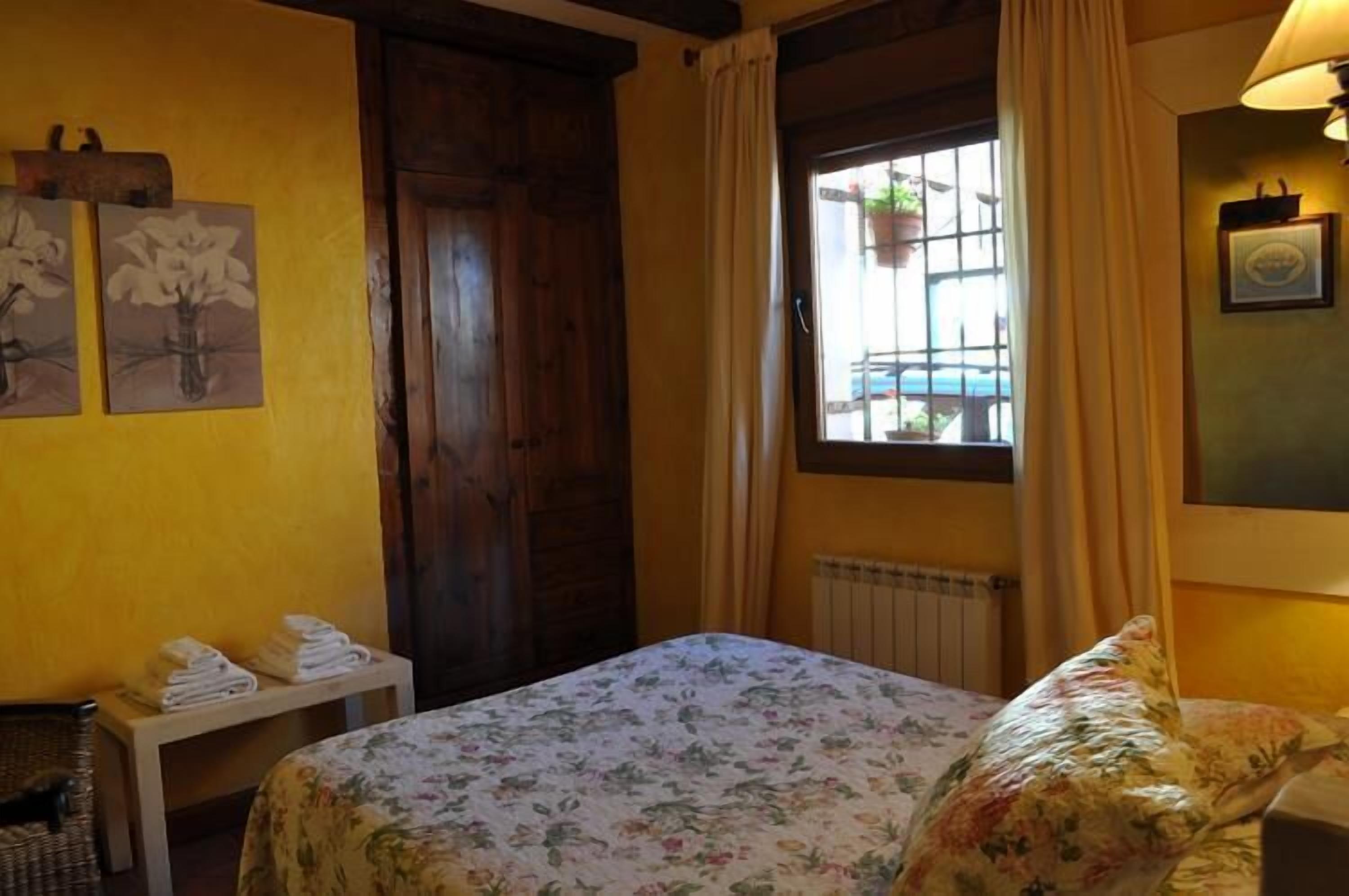A room with a bed, a window with curtains, a radiator, and a wall with framed artwork.