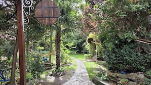 A stone pathway leading through a lush garden with a wooden sign and a metal fence. - Hospedium Hacienda Las Cavas (Olmedo)