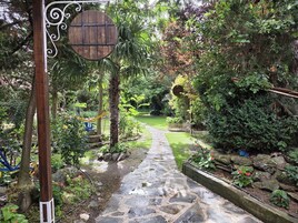 Un sendero de piedra serpentea por un exuberante jardín con un letrero de madera y una cerca de metal.