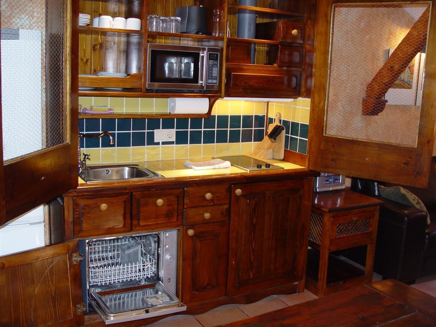 Una cocina compacta con gabinetes de madera, un microondas, un fregadero y un lavavajillas.