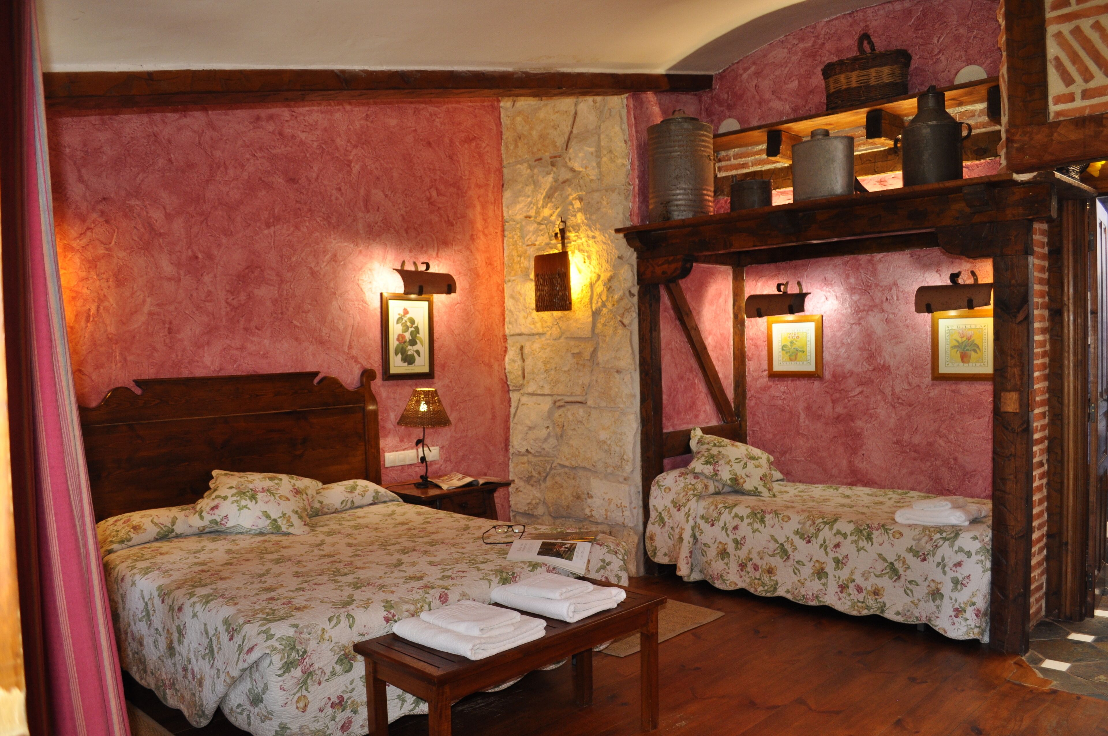 Une chambre avec deux lits, un banc en bois, un mur en pierre et une étagère contenant des ustensiles de cuisine.