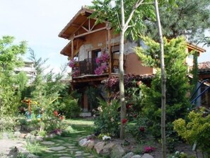 Ein rustikales Holzhaus mit Balkon, geschmückt mit Blumen, umgeben von üppigem Grün und einem Steinweg.