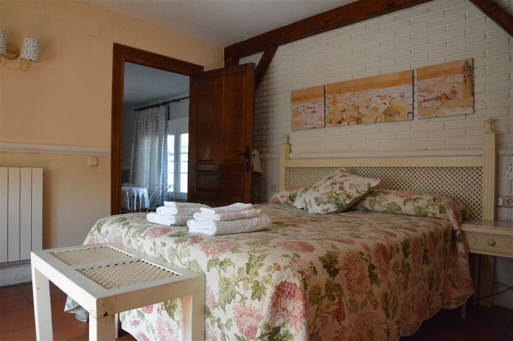 A bedroom with a floral bedspread, a wooden headboard, and a view of the outside through an open door.