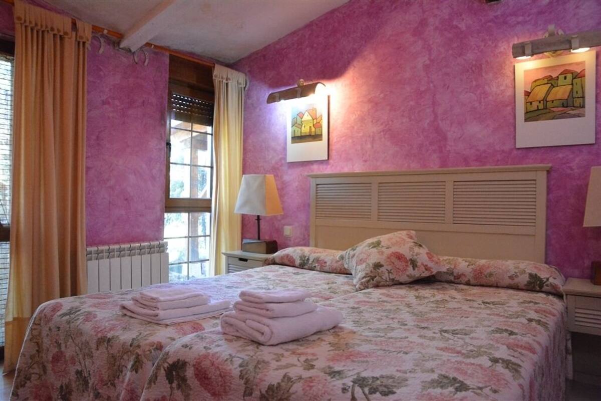 Een slaapkamer met een bed, een raam met gordijnen, een radiator en twee wandlampen.