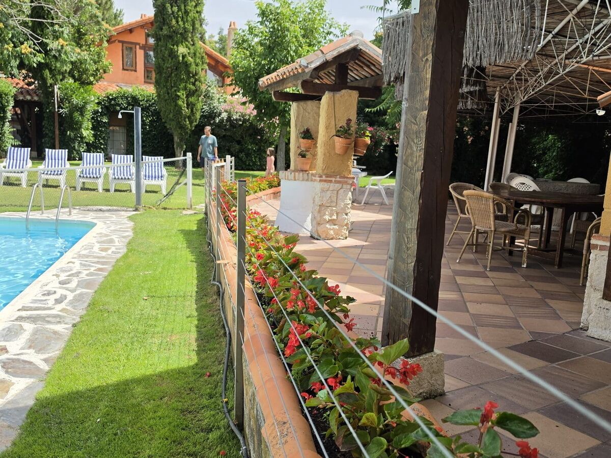 A poolside area with a stone-lined pool, a grassy lawn, and a seating area with chairs and a table.