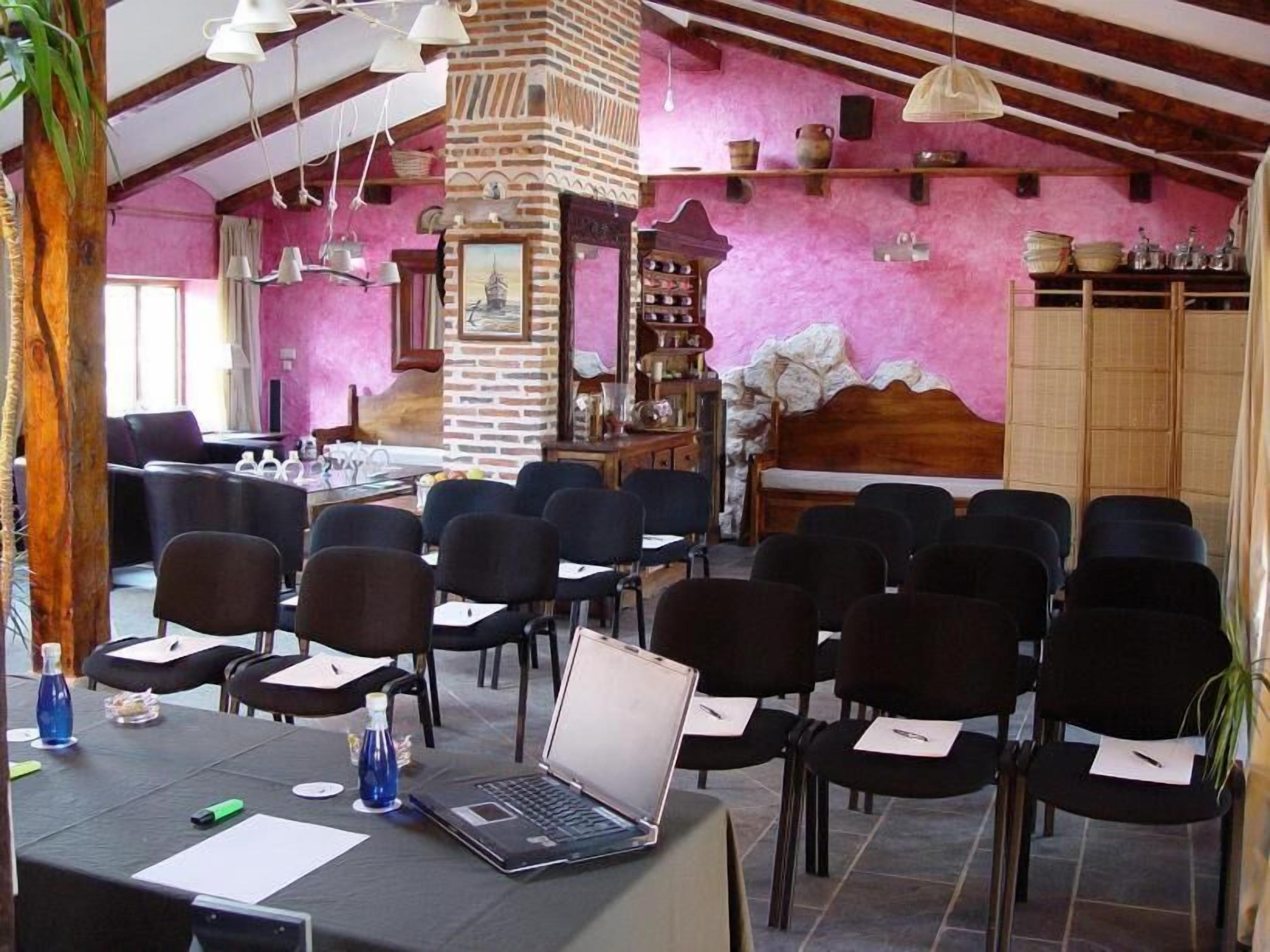Une salle de conférence avec un ordinateur portable posé sur une table, des chaises disposées pour les participants et un pilier en briques orné d’un tableau.