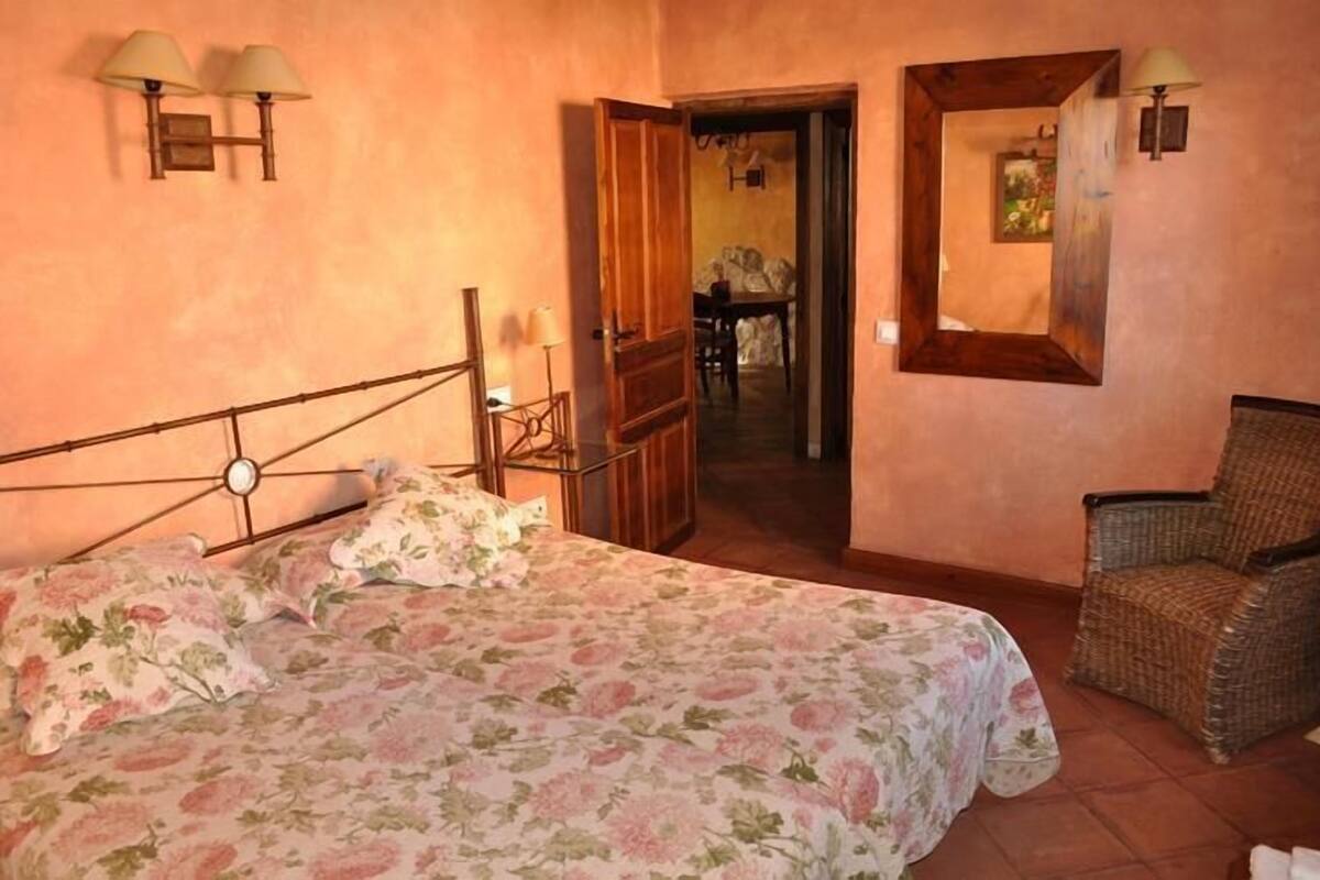 Een slaapkamer met een bed, een stoel en een deur die leidt naar een eethoek.