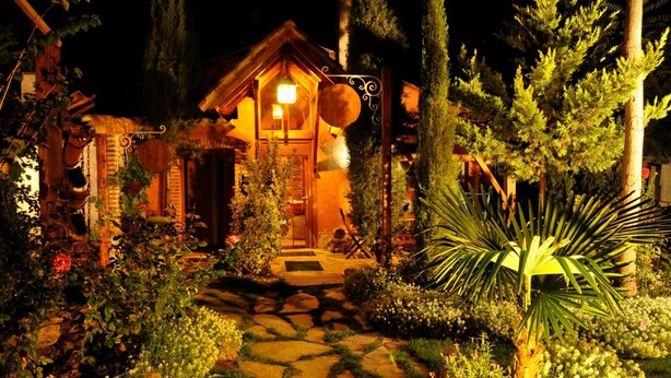 A rustic wooden cabin with a stone pathway leading to the entrance, surrounded by lush greenery and a well-lit garden. - Hospedium Hacienda Las Cavas (Olmedo)