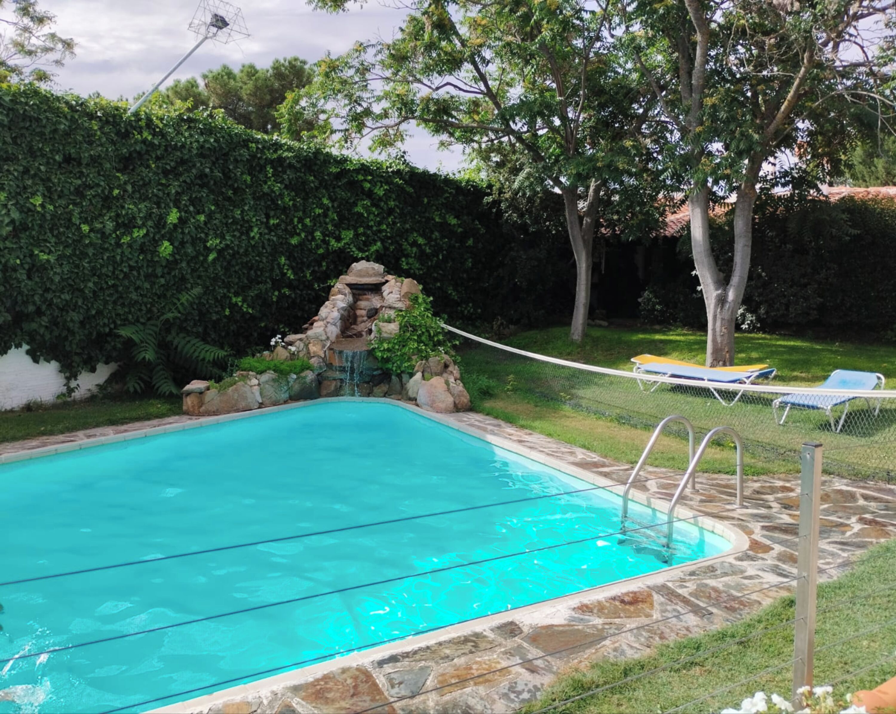 Una piscina amb un marc de pedra, una cascada petita i una cadira espanyola.