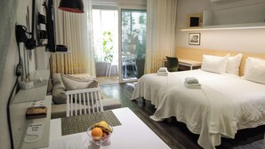 Quarto de hotel com duas camas, uma mesa com cadeira, uma luminária de mesa, uma mesinha com uma fruteira e uma janela com cortinas.