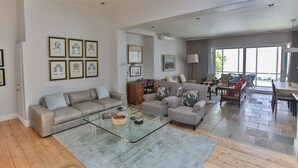 Uma sala de estar espaçosa com sofá, mesa de centro de vidro e área de jantar com cadeiras e mesa.