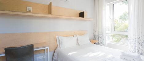 Una habitación de hotel con cama, escritorio y ventana con cortinas.