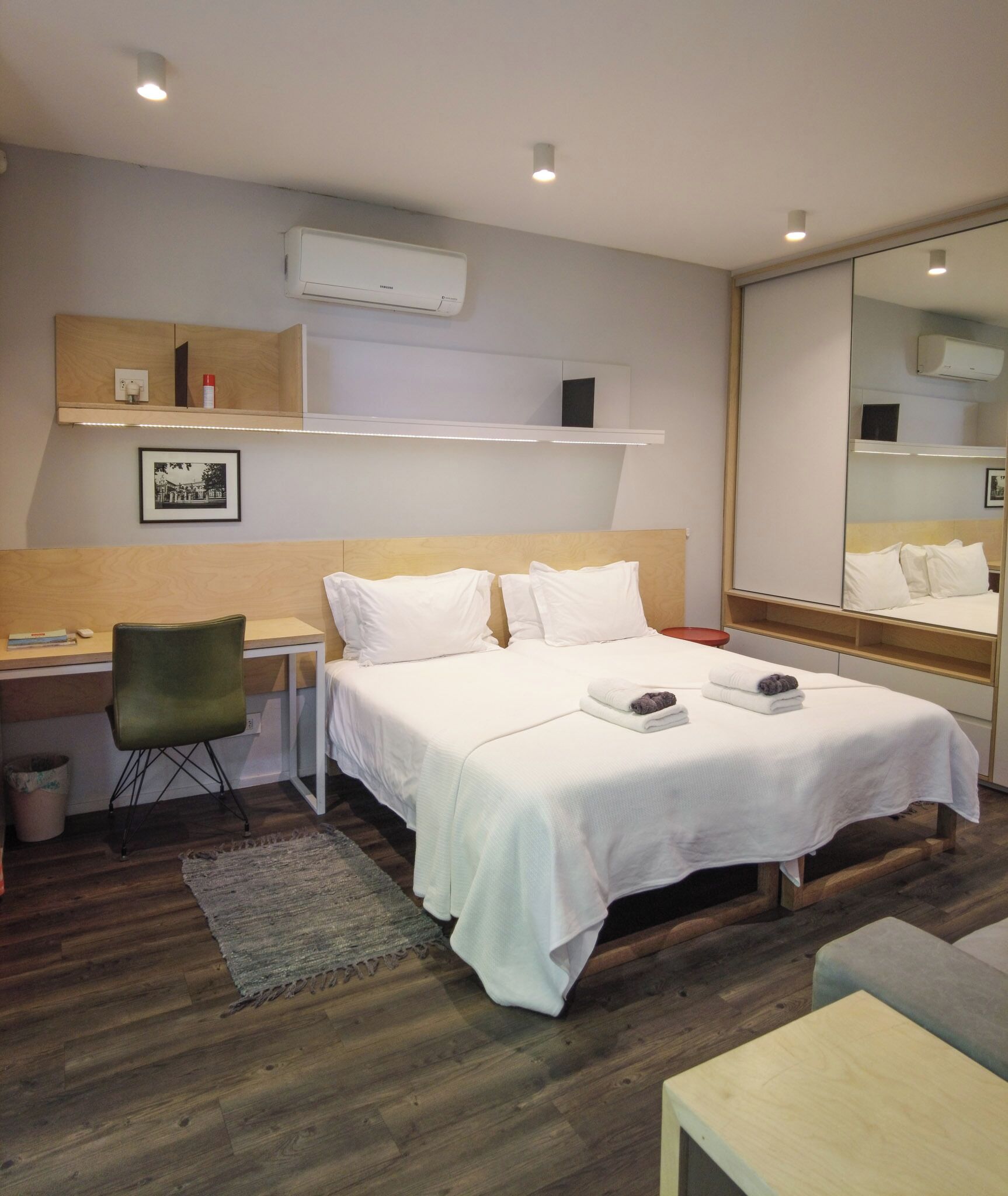 A hotel room with a bed, a desk, a chair, a small rug, and a mirror.