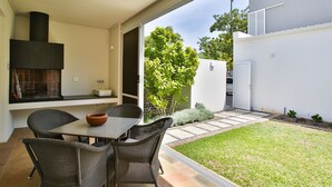Um pátio externo com móveis de vime, uma mesa e uma lareira embutida.