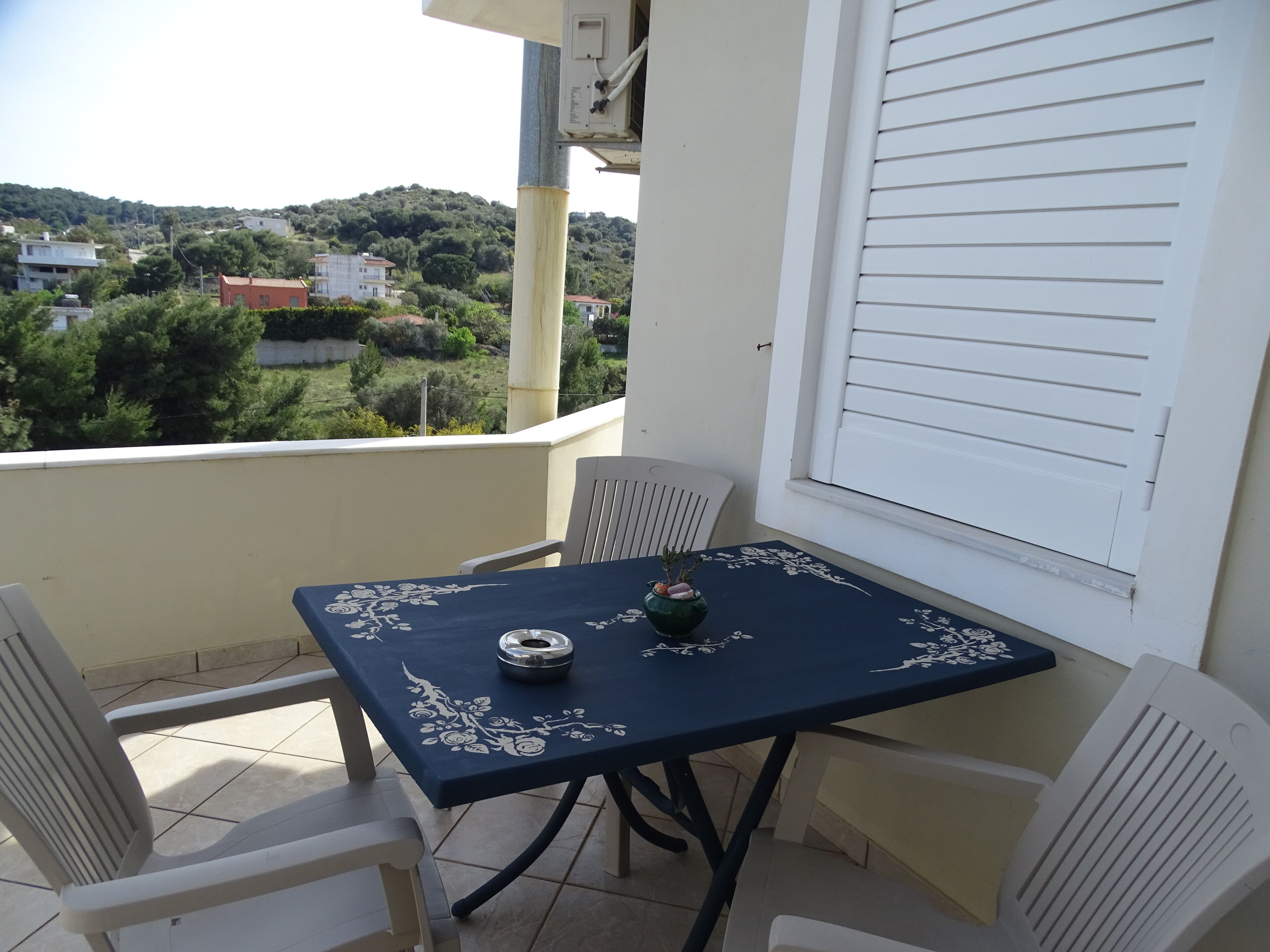 Een balkon met een tafel en stoelen, met uitzicht op een heuvel waarop gebouwen staan.