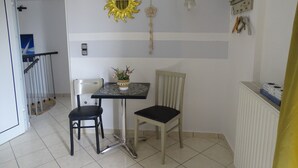 A small dining area with a table and two chairs, a decorative wall hanging, and a radiator. - Artemis GreenHill (Spata-Artemida)