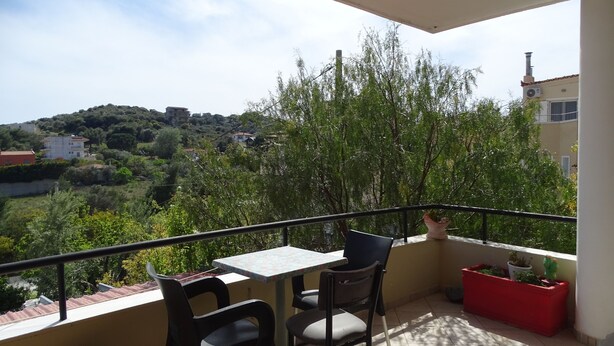 A balcony with a table and chairs, overlooking a hillside with buildings and trees. - Artemis GreenHill (Spata-Artemida)
