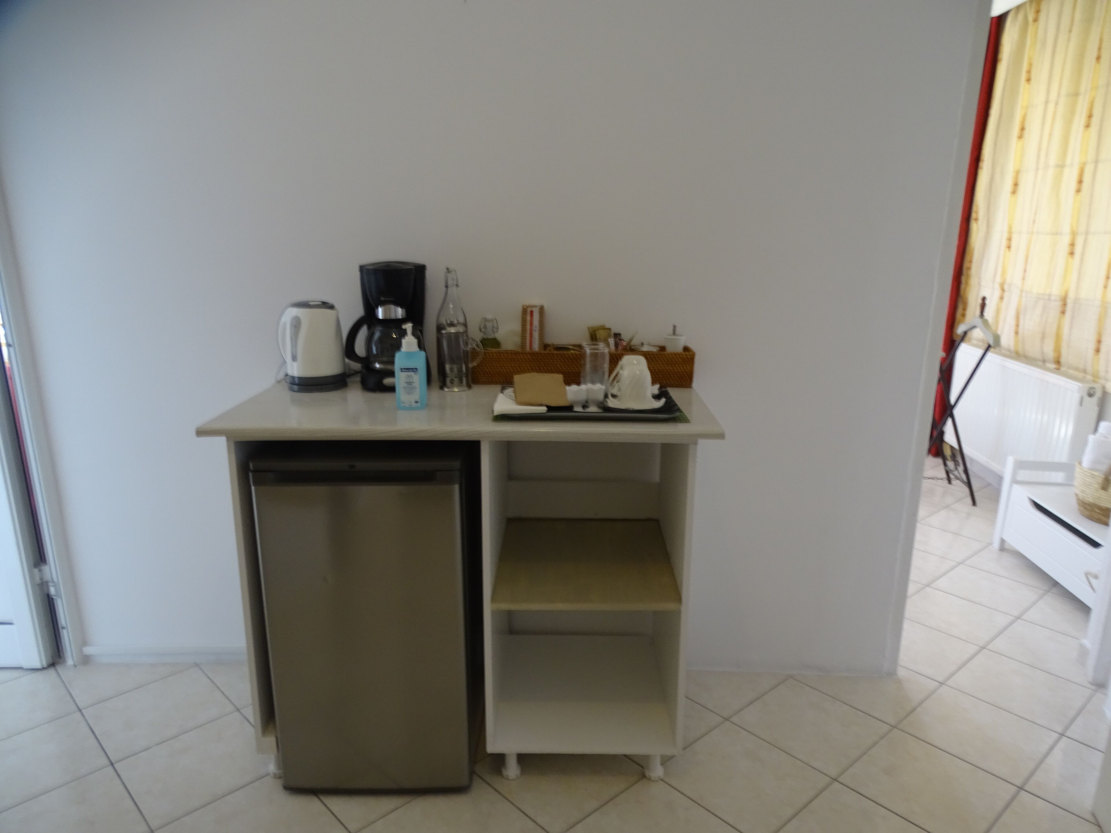 Een kleine keuken met een koelkast, koffiezetapparaat en een klein plankje.