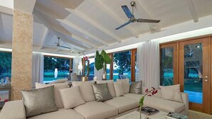 A modern living room with a beige sectional sofa, a coffee table, and a ceiling fan. - Villa Emily (La Romana)