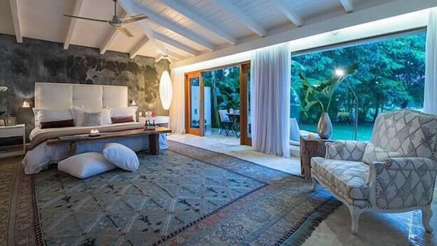 A spacious bedroom with a large bed, a ceiling fan, and a view of a lush garden through a glass door. - Villa Emily (La Romana)
