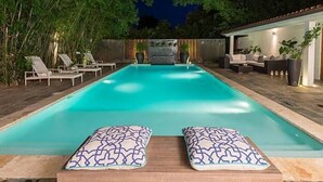 A rectangular swimming pool with two lounge chairs and cushions in the foreground. - Villa Emily (La Romana)