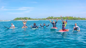 A group of people on surfboards in the ocean with a beach and greenery in the background.