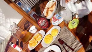 A breakfast table with various food items, including pancakes, orange slices, and a bottle of chocolate syrup. - Bitos GH (Himmafushi)