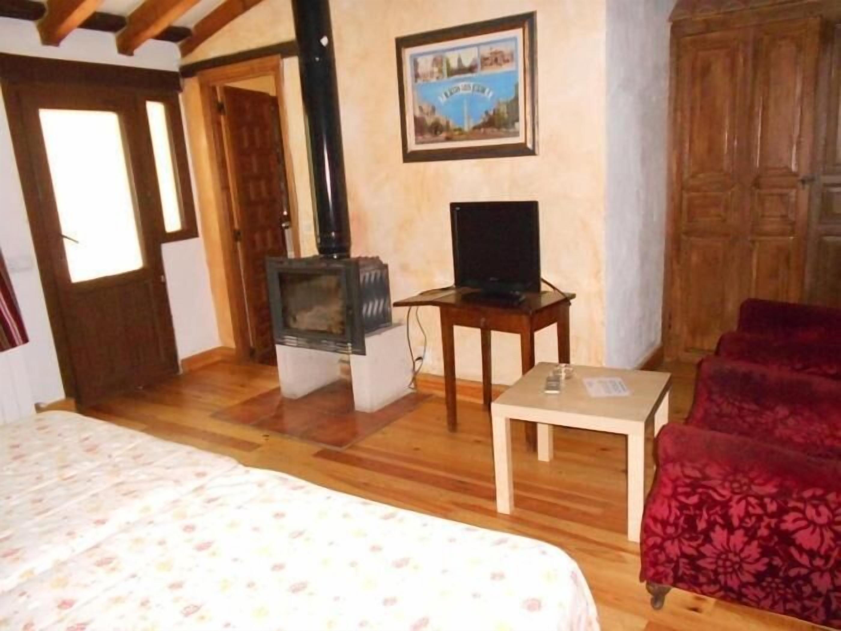 Una habitación con una cama, un televisor sobre una mesa de madera, un sofá rojo y una chimenea.