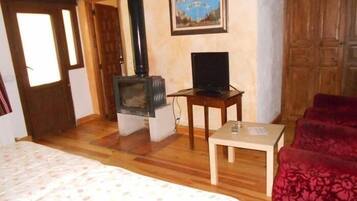 Una habitación con una cama, un televisor sobre una mesa de madera, un sofá rojo y una chimenea.